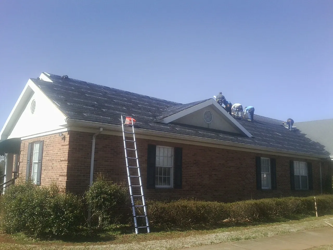 Crew tearing shingles off a brick ranch roof with a ladder set — Metal Roof Repair work by our crew in Brookfield