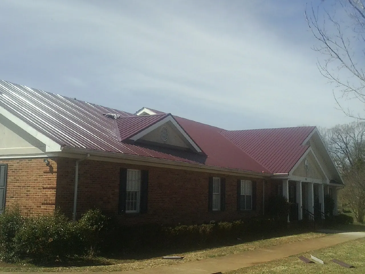 Red metal roof with gabled entries on a long brick building, from a Hail Damage Roof Repair job in Brookfield